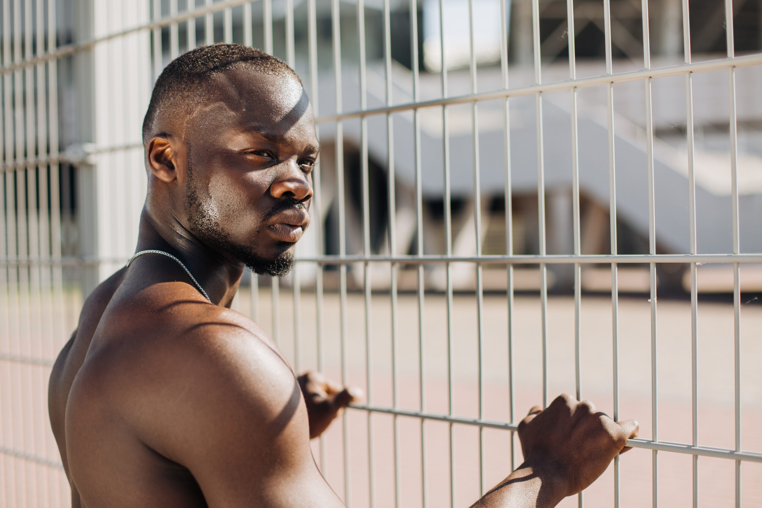 seductive african american man with muscels poses with naked chest before fence scaled